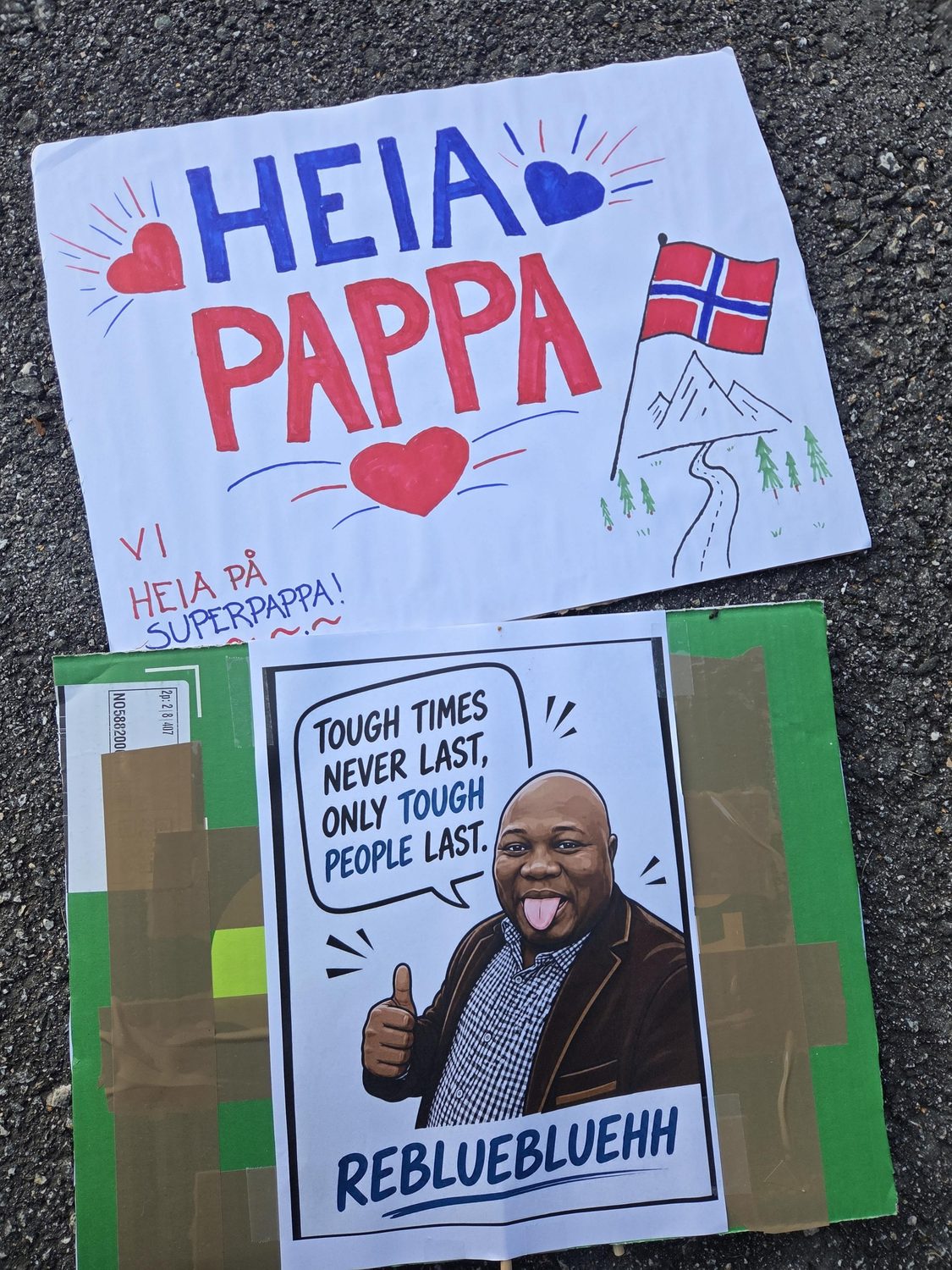 To hjemmelagde heiaplakater på asfalten: «Heia pappa» og «Tough times never last, only tough people last».