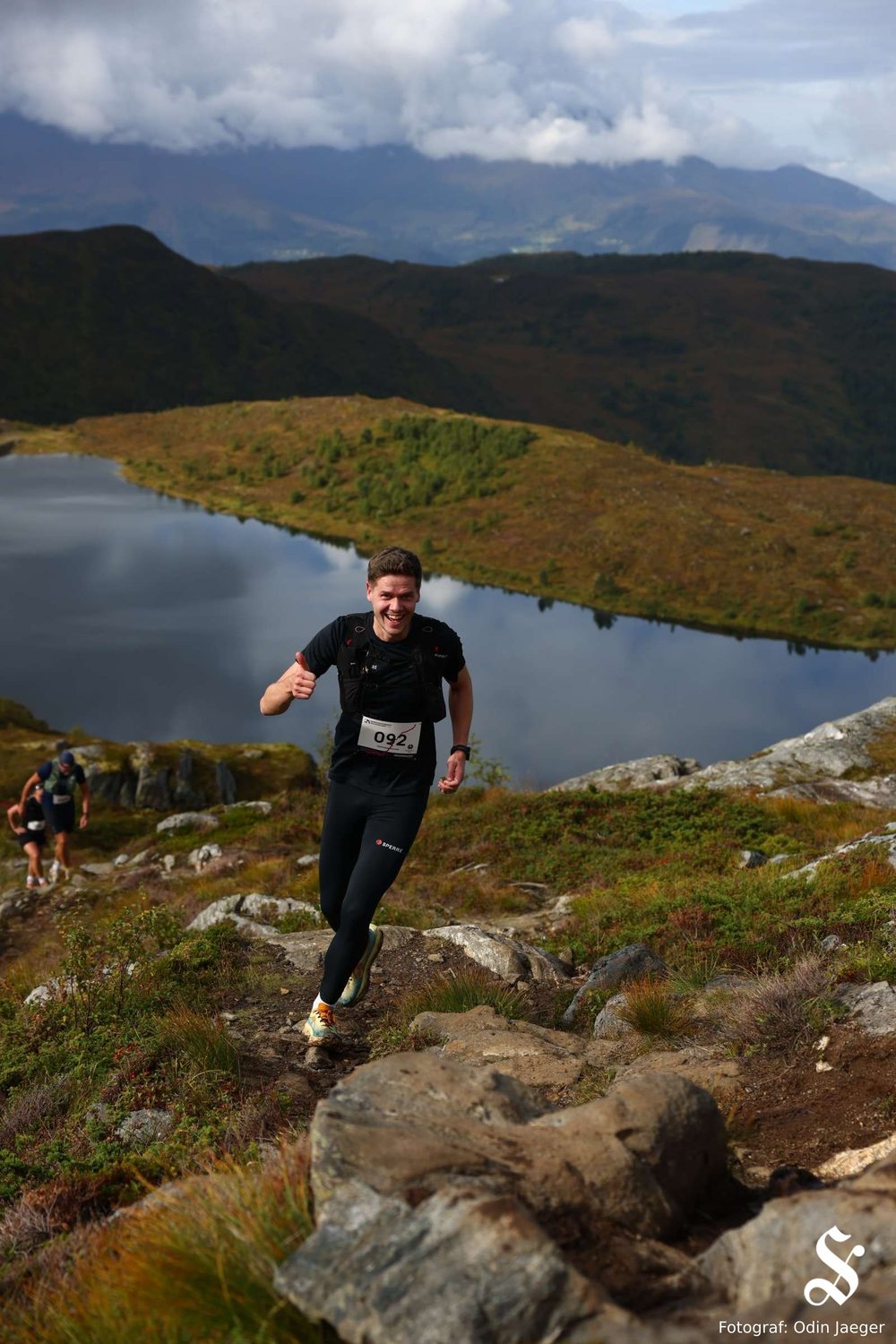 Magnus løper opp mot toppen forbi Dinglavatnet, med fjell og skyer i bakgrunnen.